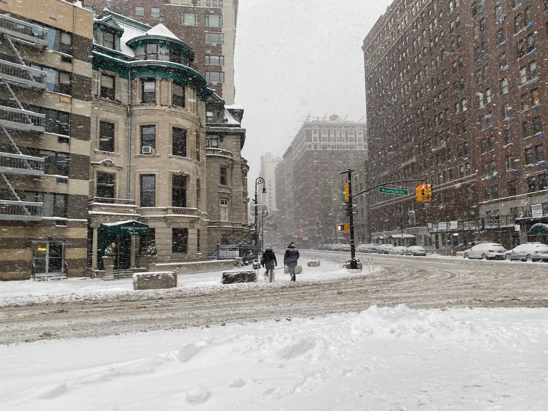 The plowed but slushy intersection of Riverside and 72nd Street, with snow falling and two people talking on the sidewalk